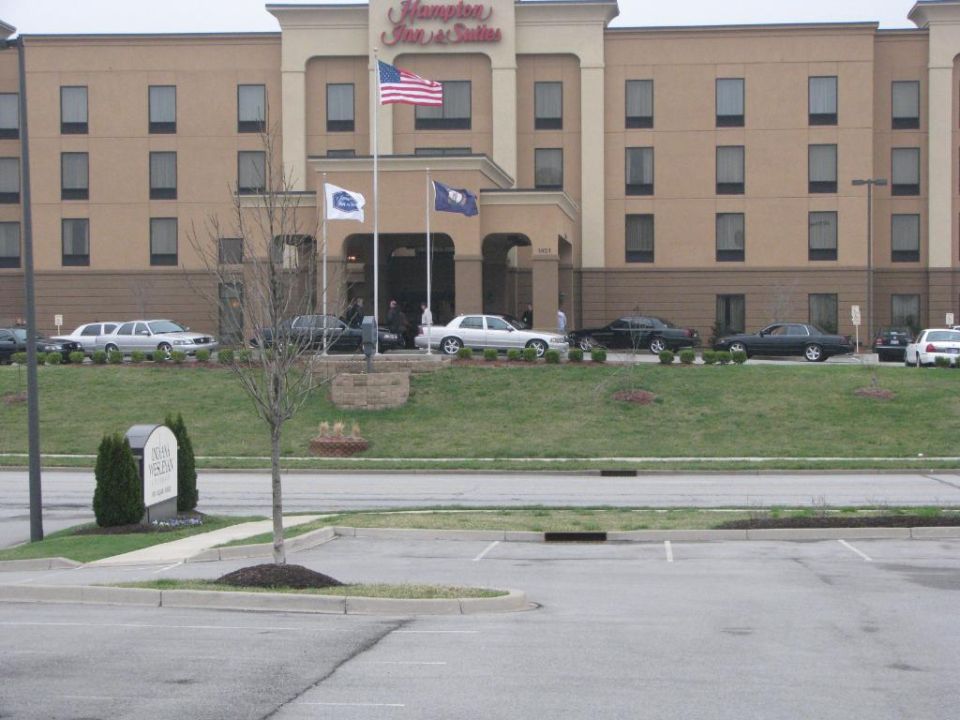Cars parked on a grassy slope in front of a Hampton Inn & Suites