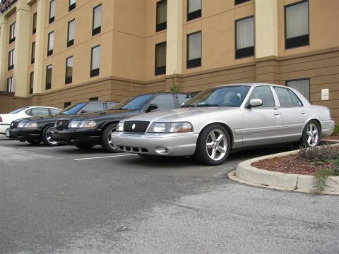 2003 Mercury Marauder - Several sedans are lined up in a parking lot in front of a hotel building.