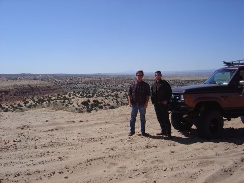 1986 Ford Bronco II - Two men stand beside a brown 1986 Ford Bronco II with a roof rack, parked in a desert landscape.