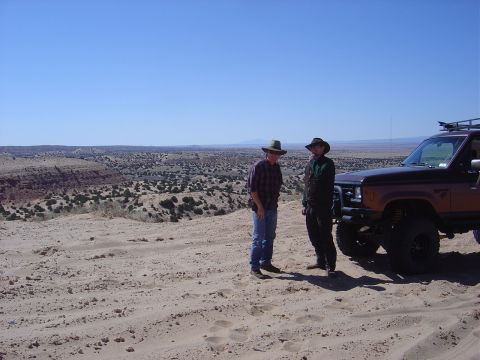1986 Ford Bronco II - Two men stand in a desert landscape next to a modified SUV under a clear blue sky.