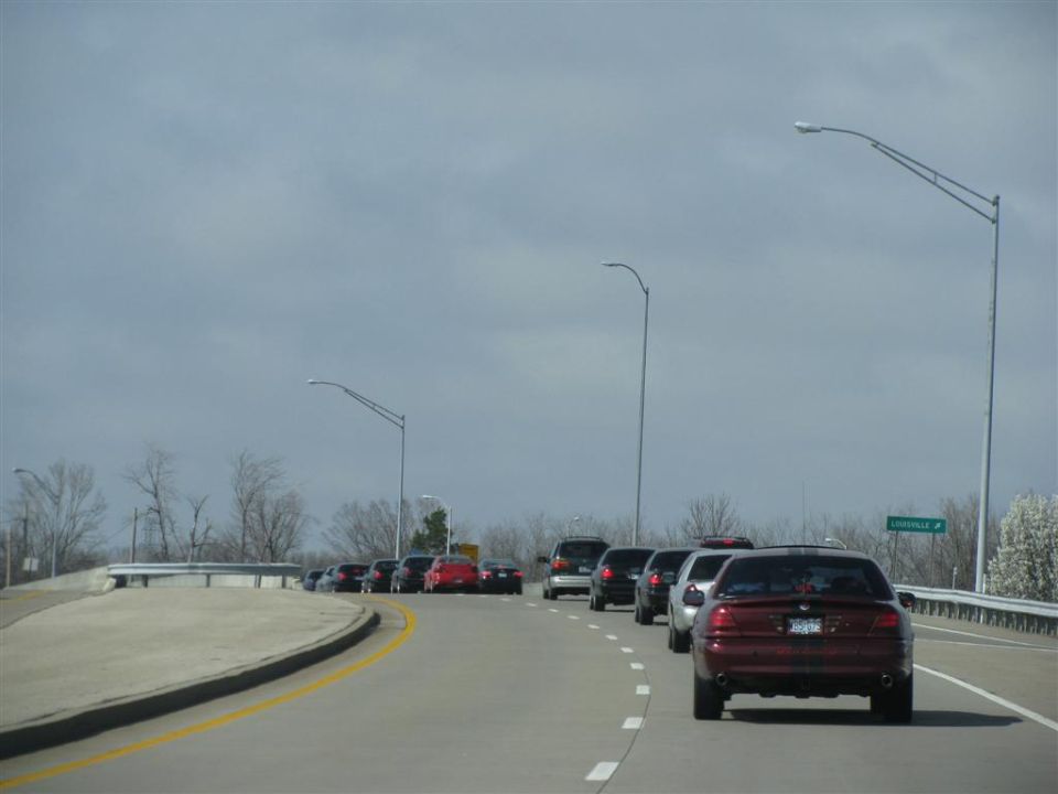 Several cars driving on a highway, with a red sedan in the foreground