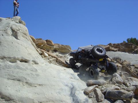 1986 Ford Bronco II - A modified off-road vehicle navigates a steep, rocky incline under a clear blue sky.