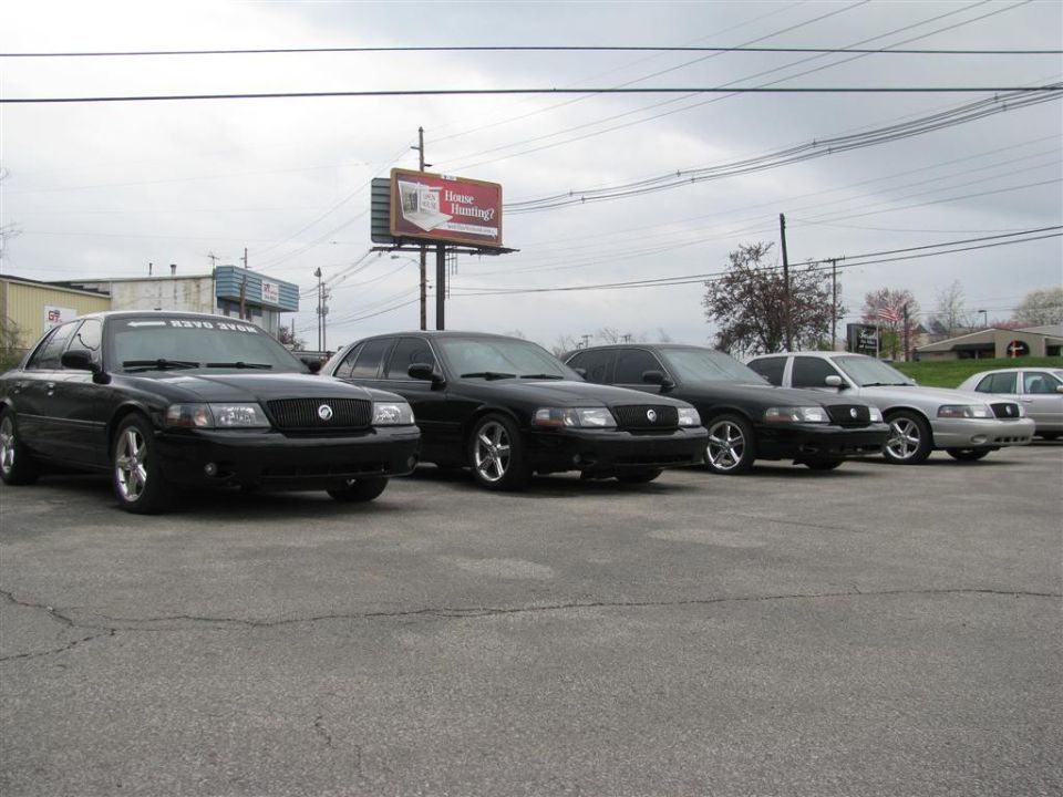 Several black and silver sedans parked in a lot, one has a banner on the windshield