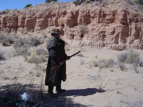 1986 Ford Bronco II - A man dressed as a cowboy stands in a dry, desert environment with a rifle.