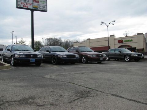 2003 Mercury Marauder - A group of four 2003 Mercury Marauders are gathered in a parking lot outside a commercial building.