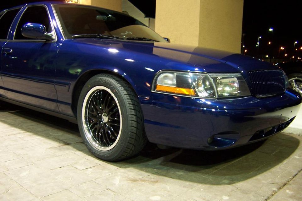 Front fender and black wheel of a blue Ford sedan at night