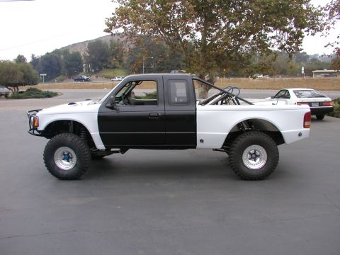 1984 Ford Bronco - Side view of a custom pickup truck with off-road modifications and a roll bar.