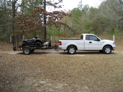 2004 Ford F-150 - White 2004 Ford F-150 tows an ATV on a trailer through a wooded area.