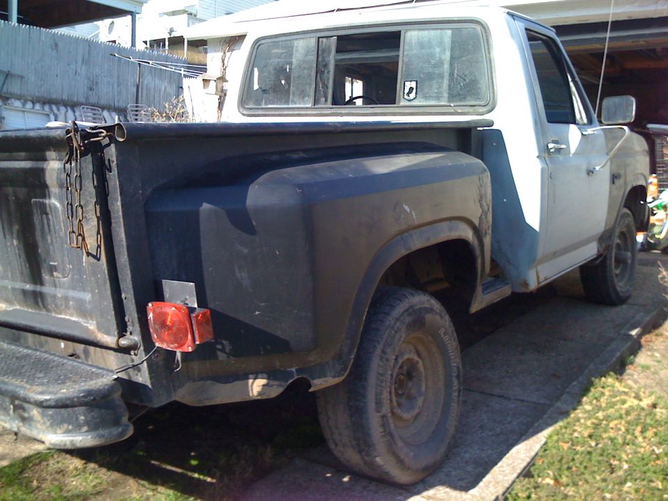 Rear quarter view of a white and blue Ford F-150 pickup truck, showing the bed and passenger side