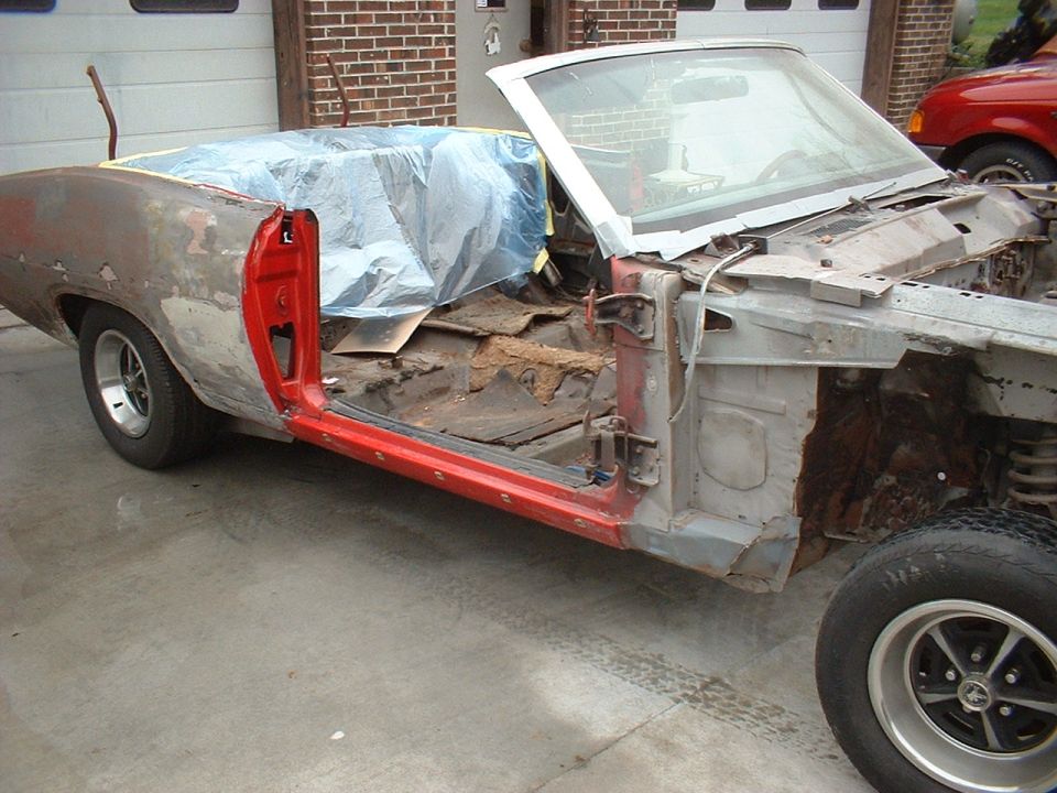 classic car body stripped down, showing rust and interior damage, covered with plastic sheeting