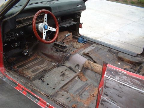 1970 Ford Torino - The interior of a 1970 Ford Torino shows significant rust and wear, with an aftermarket steering wheel and manual transmission visible.