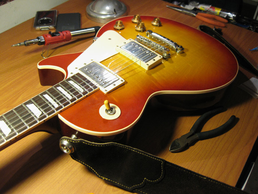 Sunburst electric guitar with tools on a wooden surface. A black guitar strap is visible