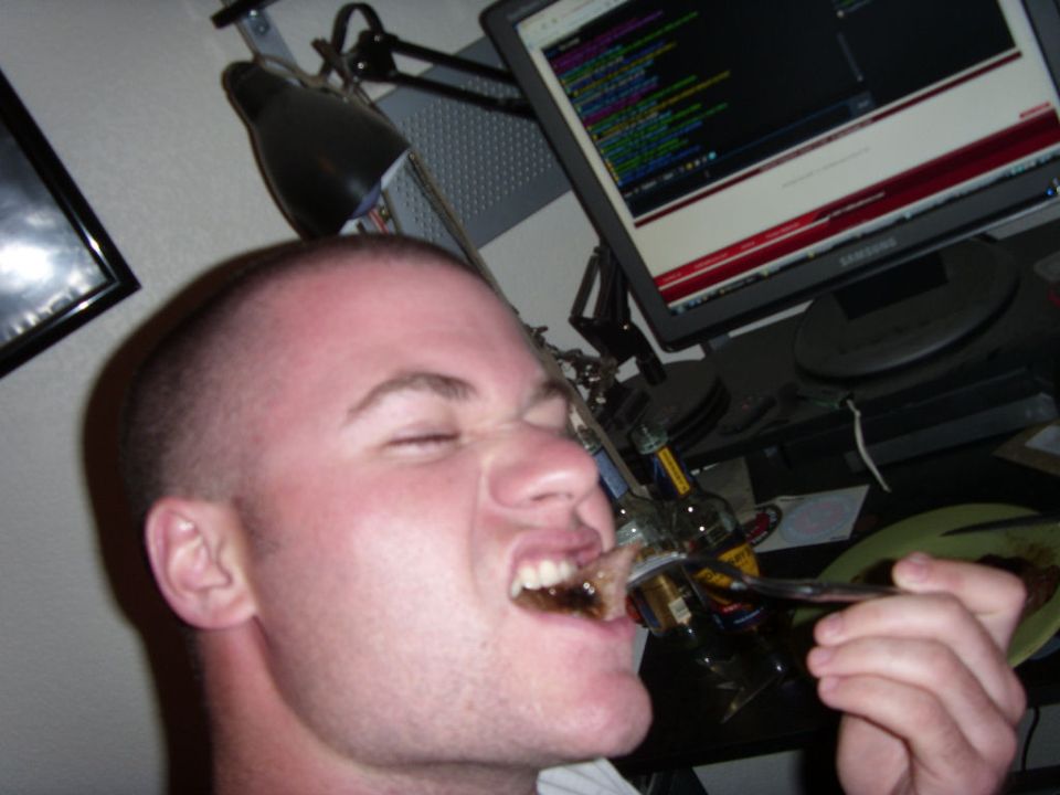 Man eating food from a fork in front of a computer screen