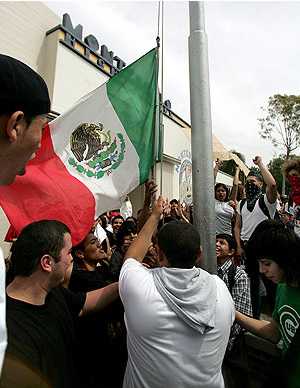 1973 Ford Torino - A group of people are gathered, raising a Mexican flag near a building with a visible sign.