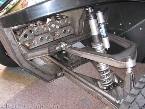 1990 Ford Bronco - close-up shows the fabricated front A-arm suspension and a Fox coilover shock of a black off-road race vehicle.