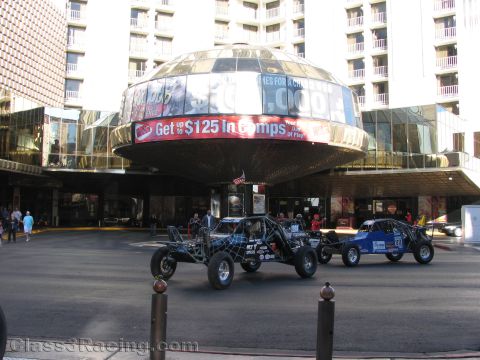 1990 Ford Bronco - Several off-road race buggies are parked on the street before a round-canopy casino hotel entrance advertising comps.