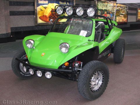 1990 Ford Bronco - bright green fiberglass dune buggy with a four-lamp roof light bar, chrome bumper lights, and BFGoodrich tires on display indoors.