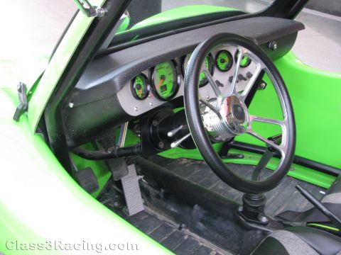 1990 Ford Bronco - Close-up of a green off-road buggy interior with a black steering wheel, chrome steering column, and round gauges in a black dash panel.