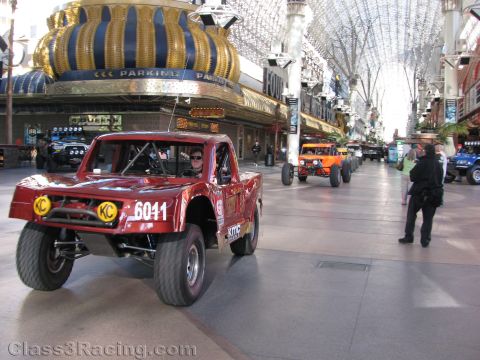 1990 Ford Bronco - dark red off-road race truck marked 6011 with KC lights rolls along a covered pedestrian street under the Fremont canopy.