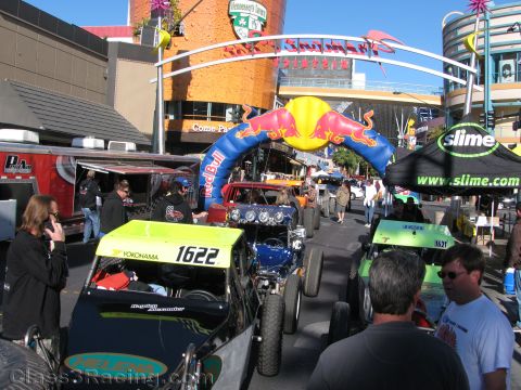 1990 Ford Bronco - busy street event with off-road race cars numbered 1622 and others, a Red Bull arch, a Slime sponsor tent, and spectators.