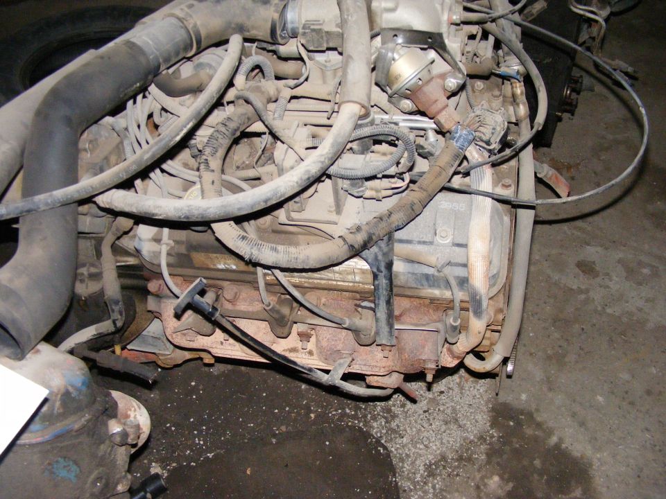 Engine bay with hoses, wiring, and spark plug wires visible. Some rust on exhaust manifold