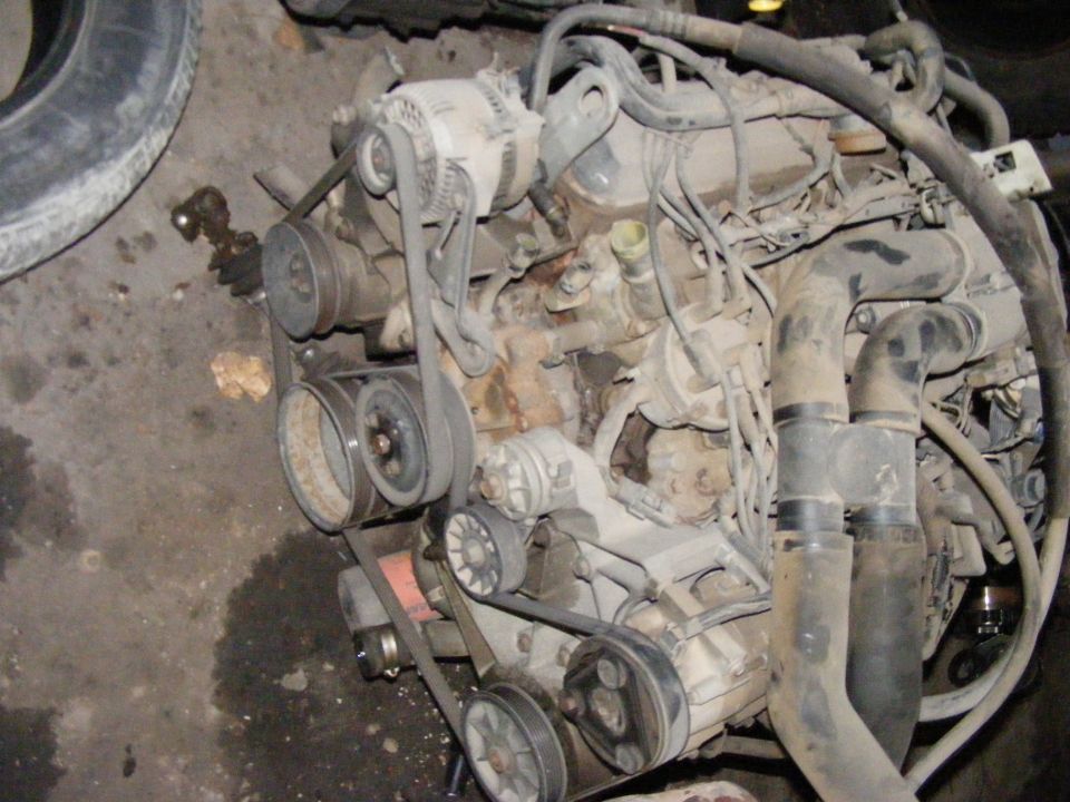 Engine with belts and pulleys, looks dirty. Tire in background