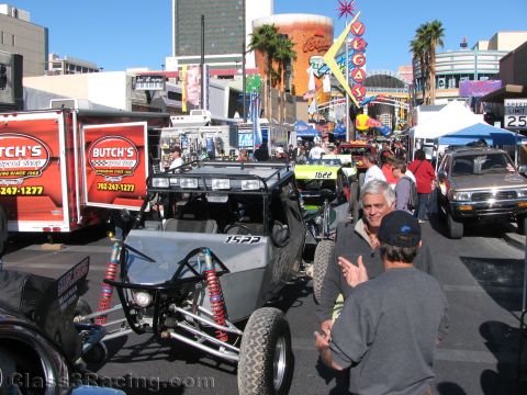 1990 Ford Bronco - crowded downtown off-road event with tube-frame buggies, trucks, a Butch's Speed Shop trailer, and Vegas signage in the background.