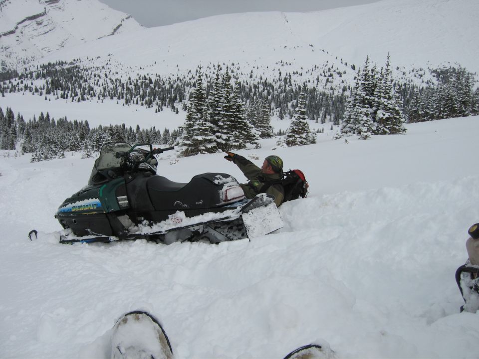 Green and black 1999 Arctic Cat Powder Special 600 EFI snowmobile partially buried in snow, with a person pointing