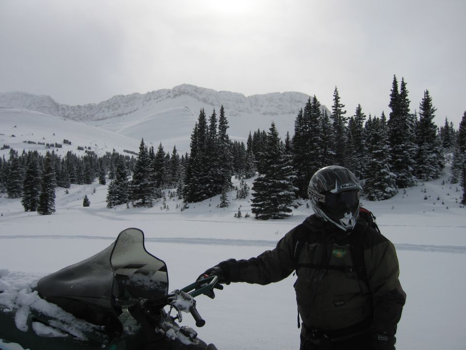 Snowmobile windshield and handlebars in a snowy mountain landscape
