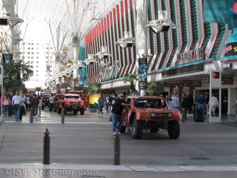 1990 Ford Bronco - orange early-Bronco-style off-road truck and a red race truck move along the covered Fremont Street Experience in Las Vegas.