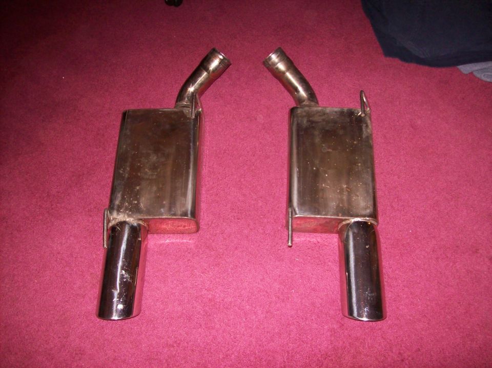 two chrome exhaust mufflers with angled tips, sitting on a red carpet