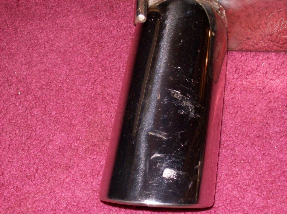 Chrome exhaust tip with scratches on a pink carpeted surface
