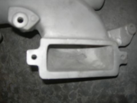 1984 Ford Bronco - This is a close-up view of a metal automotive part, likely an intake manifold, with visible mounting holes.