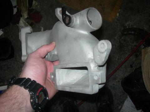 1984 Ford Bronco - An aluminum intake manifold is held for inspection, its metallic surface showing cast details and connection points.