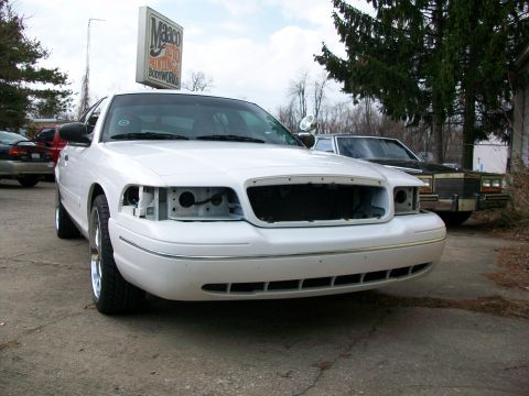 2003 Ford Crown Victoria - Front view of a white 2003 Ford Crown Victoria, missing its grille and headlights, parked outdoors.
