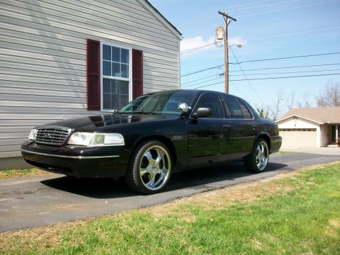2003 Ford Crown Victoria - This black 2003 Ford Crown Victoria features custom chrome wheels and is parked in front of a residential home.