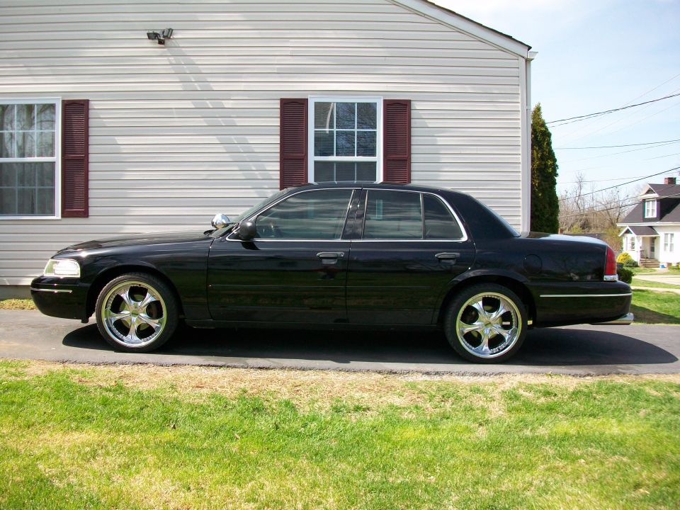 Side view of a black 2003 Ford Crown Victoria with chrome rims parked in front of a house