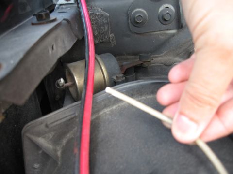 1994 Ford Bronco - A hand manipulates a thin tube near engine bay components, including a brass-colored vacuum actuator.