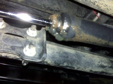 2008 Jeep Wrangler - Grimy underbody close-up of a driveshaft slip yoke and universal joint packed with fresh grease, photographed with a flash from beneath the…