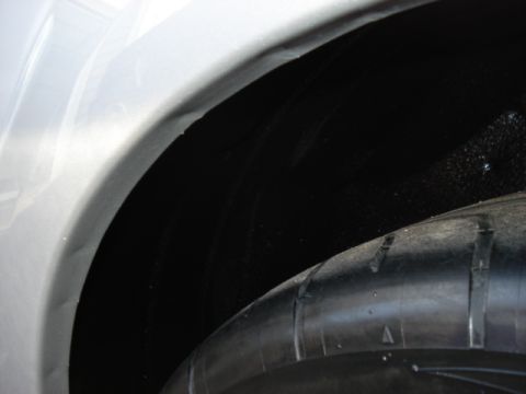 1998 Ford Taurus - A close-up view of a vehicle's wheel well and tire, with a white fender visible.