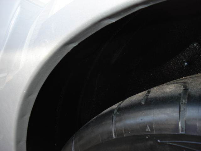 Close-up of a black wheel well and tire with a white fender above