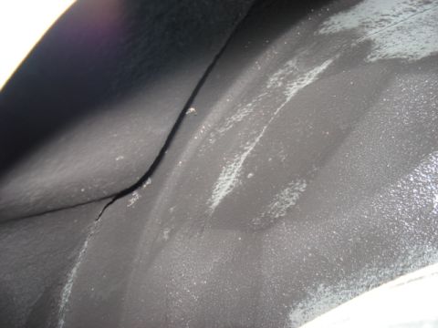 1998 Ford Taurus - Close-up view of a cracked black wheel well liner, showing texture and some white residue.