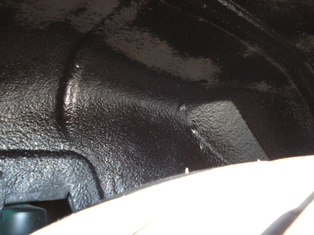 Close-up of black undercoating on a car's wheel well. A Supermotors logo is visible at the bottom right
