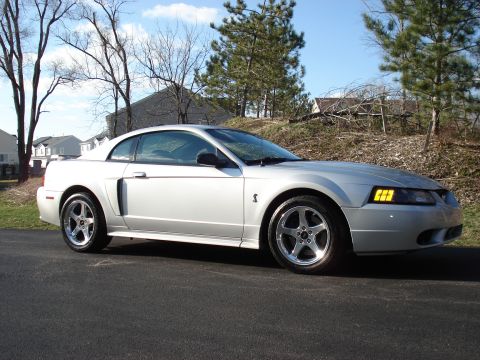 1998 Ford Taurus - This silver coupe, likely a 1999 Ford Mustang, features a distinctive side scoop and five-spoke wheels.