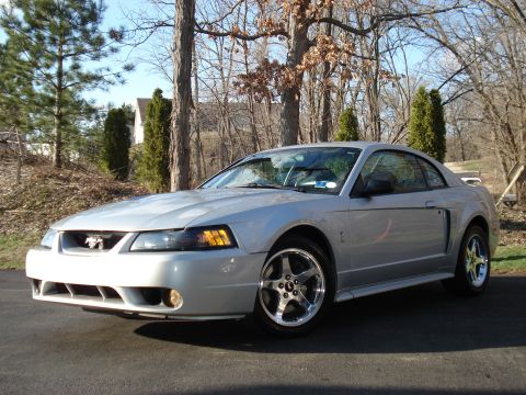 1998 Ford Taurus - This silver coupe features a distinctive horse emblem on its grille, indicating it is not a 1998 Ford Taurus.
