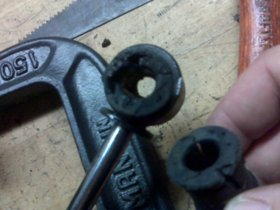 worn rubber bushings held by a c-clamp, with a saw and hammer handle visible