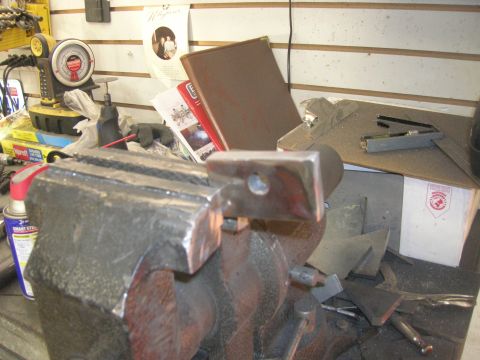 1996 Ford Bronco - A metal bracket is secured in a vise, surrounded by metal scraps and tools on a workbench.
