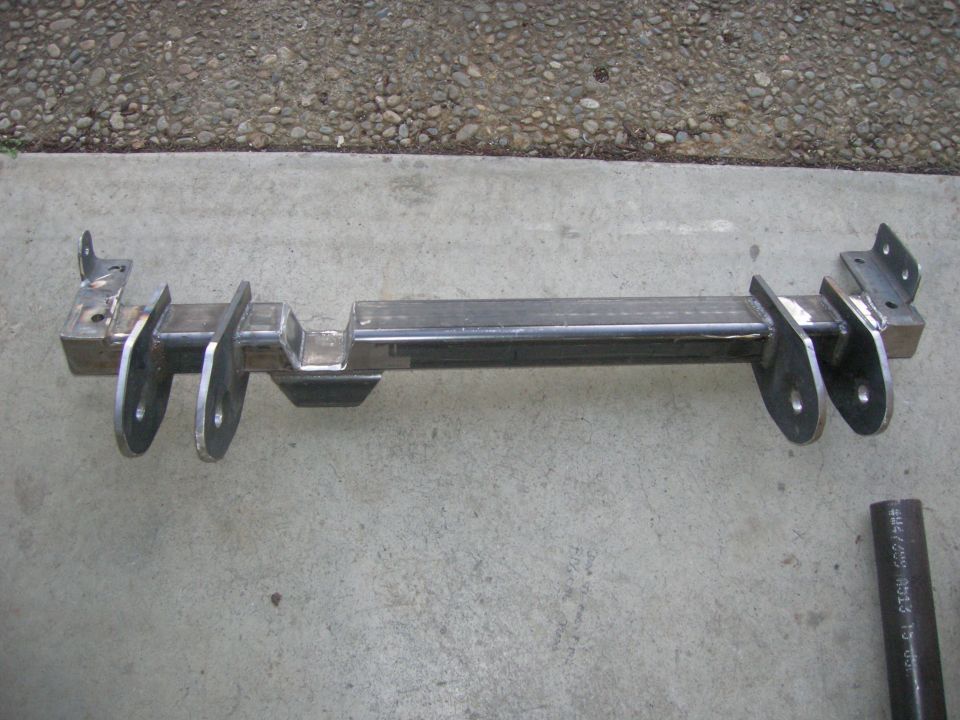 Custom metal crossmember with mounting brackets and holes, lying on concrete