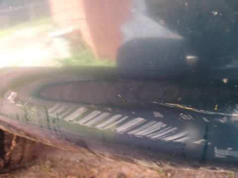 1995 Ford Taurus - A close-up shot focuses on the lower body panel of a vehicle, showing reflections and minor damage.