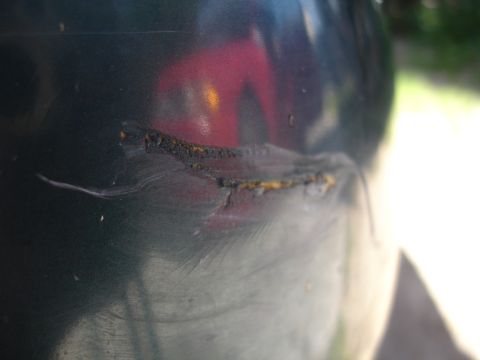 1995 Ford Taurus - A close-up of a damaged car panel shows a significant scratch with rust, obscuring any identifying details.